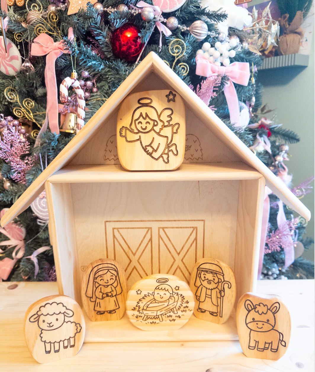 Wooden nativity scene figures in a house-shaped box with a Christmas tree in the background