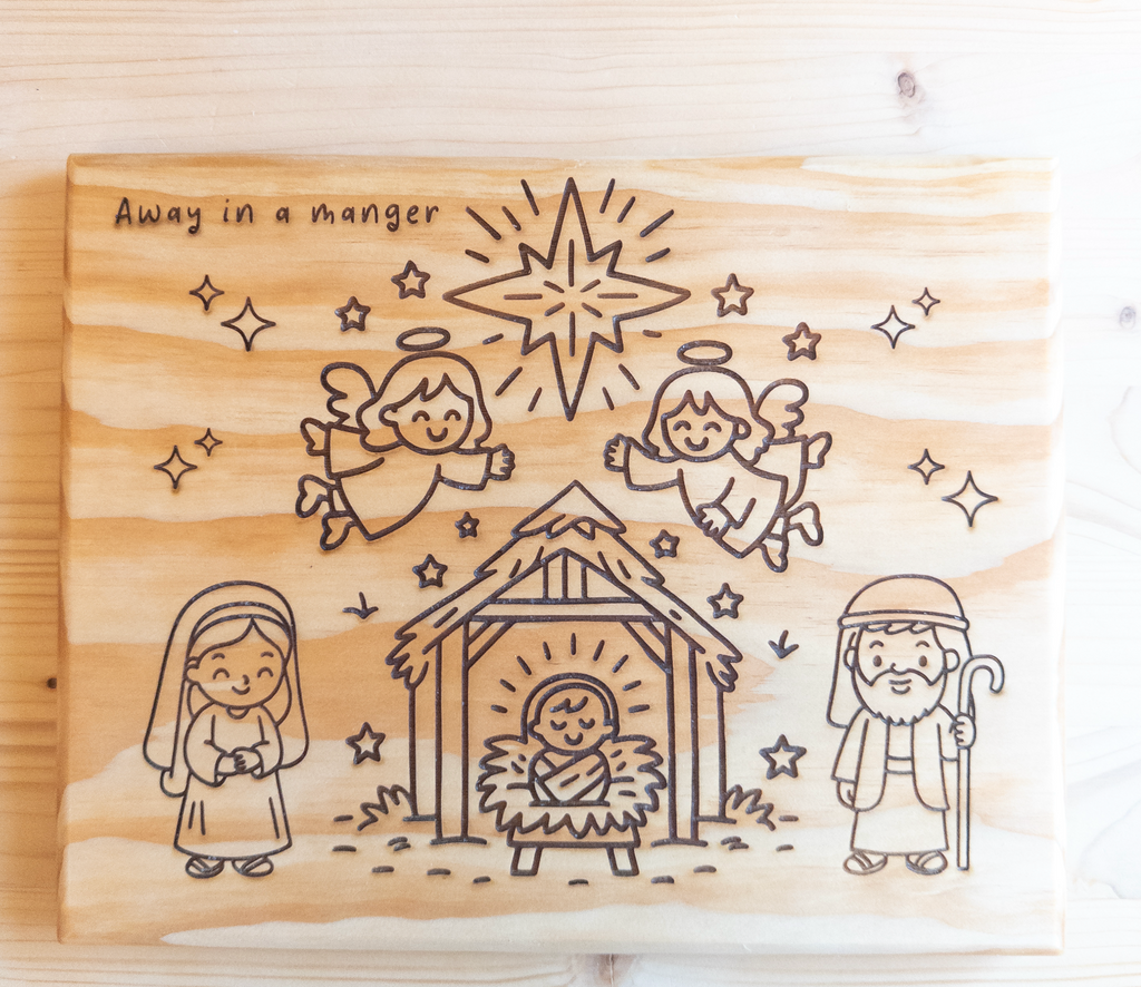Wooden plaque with engraved nativity scene and text 'Away in a manger' on a wooden background.
